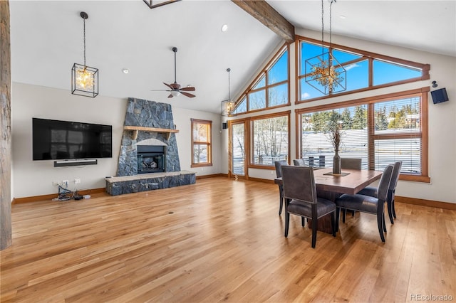 dining room featuring beam ceiling, high vaulted ceiling, a stone fireplace, light wood finished floors, and baseboards