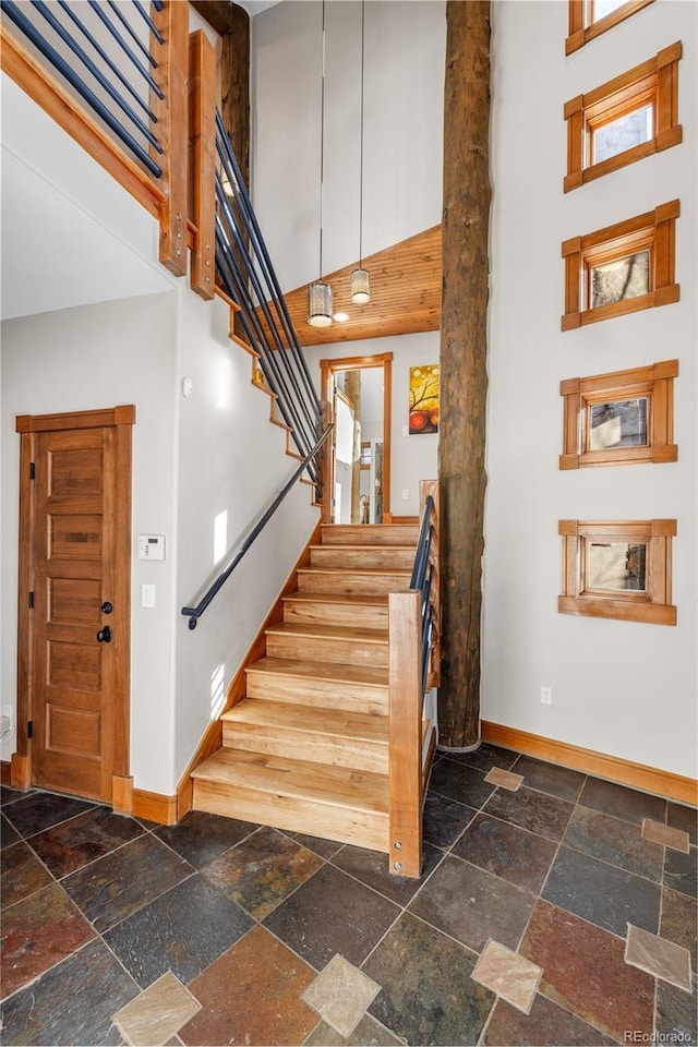 staircase with stone tile floors, baseboards, and a high ceiling