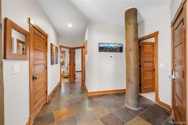 hall with decorative columns, baseboards, and stone tile flooring