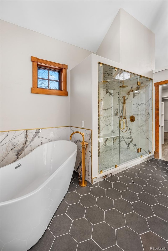 bathroom with tile walls, a freestanding tub, a marble finish shower, and wainscoting