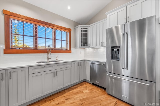 kitchen with backsplash, vaulted ceiling, light wood-style flooring, appliances with stainless steel finishes, and a sink