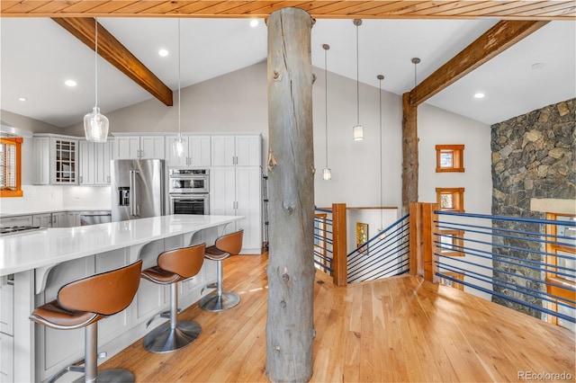 kitchen with a breakfast bar, vaulted ceiling with beams, light wood-type flooring, and appliances with stainless steel finishes