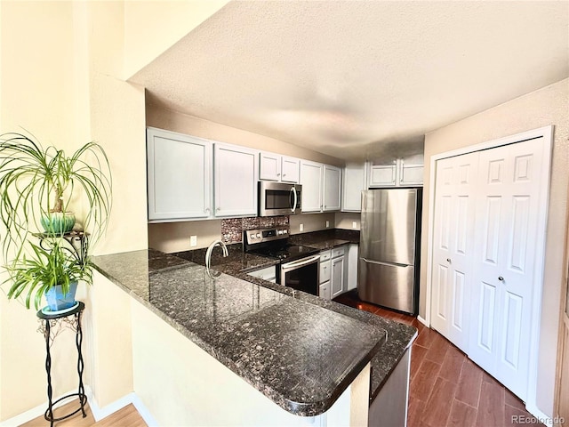 2575 S Syracuse Way Unit F301, Denver, CO 80231 - kitchen with stainless steel appliances, dark wood-type flooring, a peninsula, dark stone countertops, and a textured ceiling