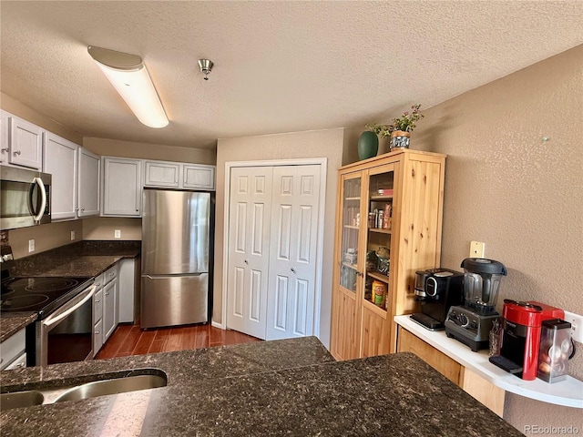 2575 S Syracuse Way Unit F301, Denver, CO 80231 - kitchen with stainless steel appliances, dark wood finished floors, a textured wall, a textured ceiling, and dark stone countertops