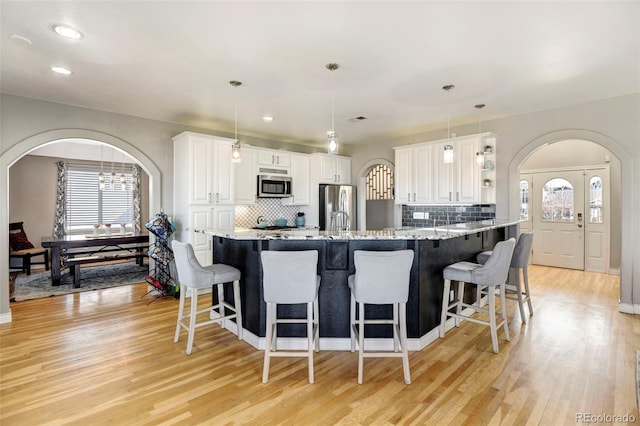 kitchen with appliances with stainless steel finishes, light wood-style flooring, a breakfast bar area, arched walkways, and recessed lighting