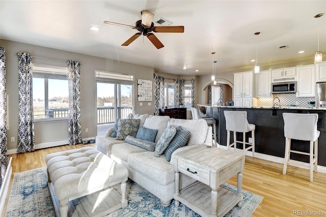 living area featuring a ceiling fan, light wood-type flooring, recessed lighting, arched walkways, and baseboards