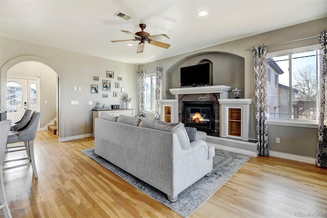living room with light wood-style floors, arched walkways, baseboards, a glass covered fireplace, and recessed lighting
