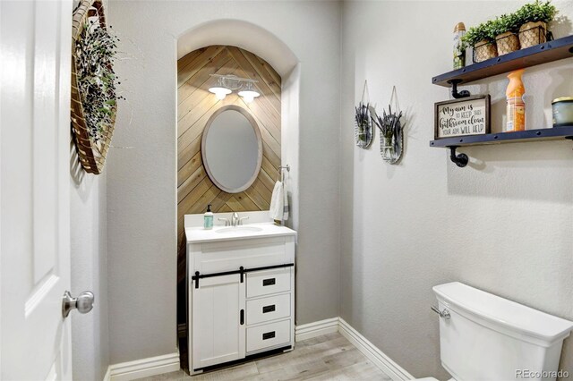 half bathroom featuring wood finished floors, vanity, baseboards, and toilet