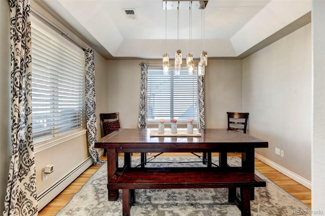 dining space with baseboard heating, a raised ceiling, light wood-type flooring, and healthy amount of natural light