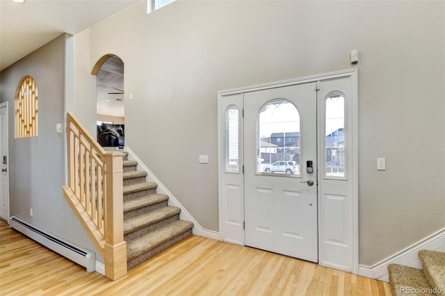 entryway featuring a baseboard radiator, stairs, wood finished floors, baseboards, and arched walkways
