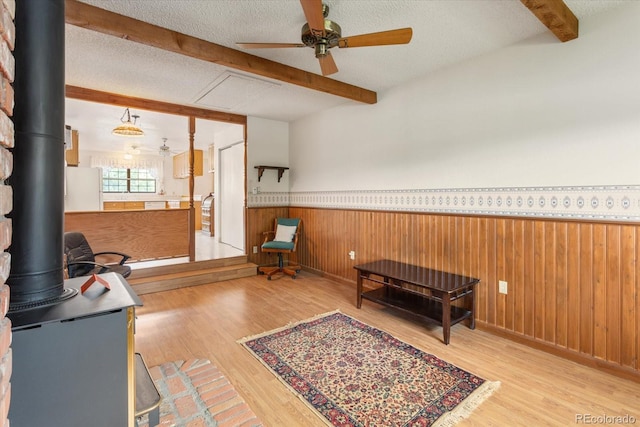 534 Crestone Ave, Salida, CO 81201 - sitting room featuring beamed ceiling, a ceiling fan, a wood stove, wood finished floors, and a wainscoted wall