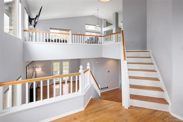 staircase with high vaulted ceiling, visible vents, baseboards, and wood finished floors
