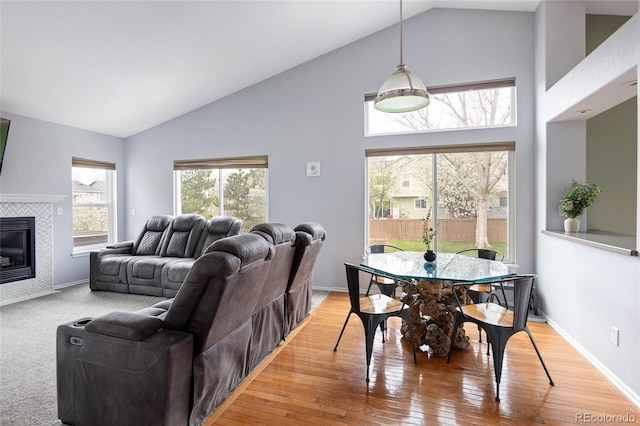 living room featuring high vaulted ceiling, a fireplace, light wood-type flooring, and baseboards