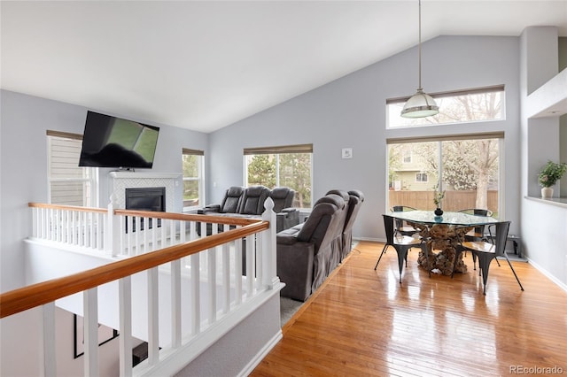 living area with high vaulted ceiling, a tiled fireplace, and light wood-type flooring