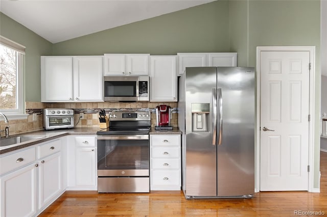 kitchen with appliances with stainless steel finishes, a sink, white cabinetry, lofted ceiling, and decorative backsplash