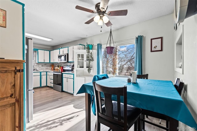 dining area featuring light wood-style flooring, a ceiling fan, and a textured ceiling