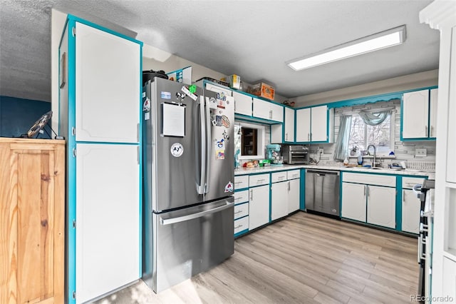 kitchen featuring light wood-style flooring, stainless steel appliances, a sink, white cabinets, and light countertops