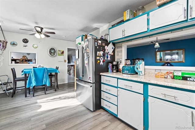 kitchen with light wood finished floors, light countertops, freestanding refrigerator, white cabinetry, and a textured ceiling