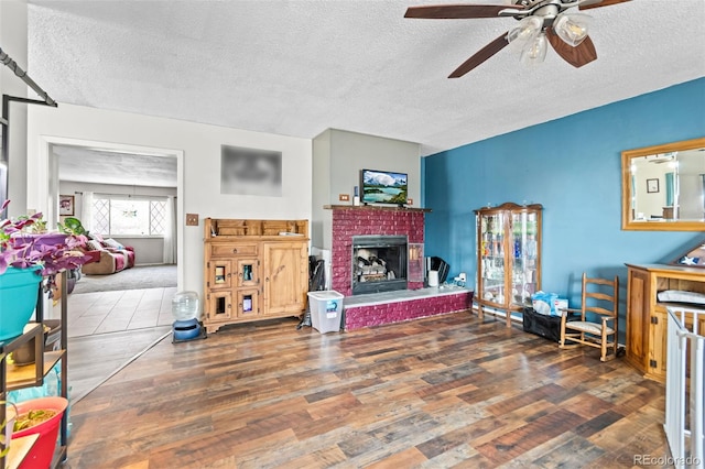 living room featuring a textured ceiling, a fireplace, wood finished floors, and a ceiling fan