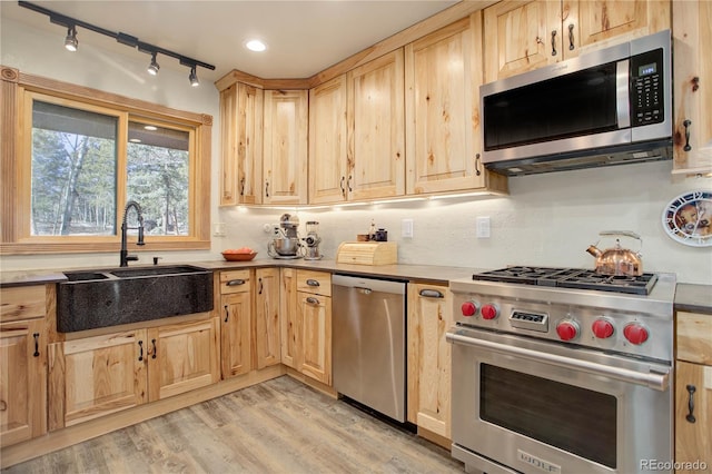 kitchen with light brown cabinets, sink, light wood-type flooring, tasteful backsplash, and stainless steel appliances