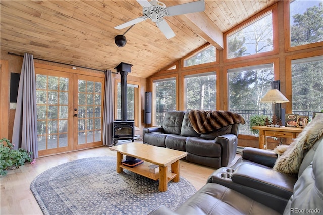 living room with lofted ceiling with beams, a healthy amount of sunlight, a wood stove, and light hardwood / wood-style flooring