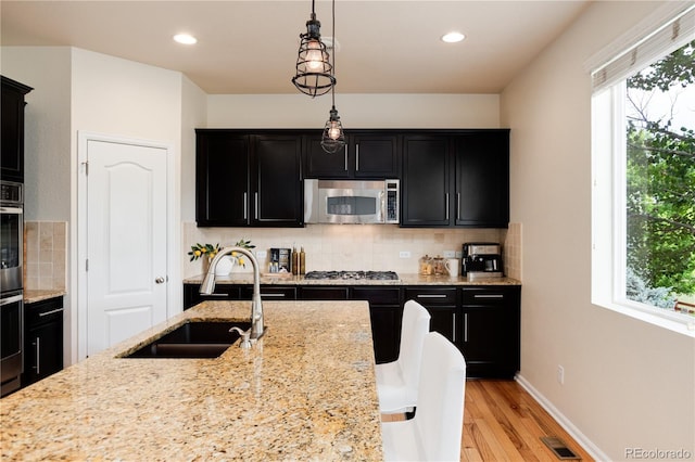 3027 Walnut Grove St, Erie, CO 80516 - kitchen with stainless steel appliances, dark cabinets, light wood-style flooring, hanging light fixtures, and decorative backsplash