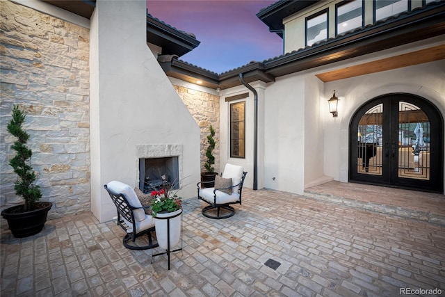 patio terrace at dusk featuring an outdoor fireplace and french doors