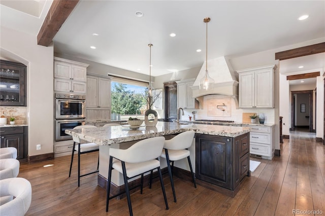 kitchen featuring backsplash, hanging light fixtures, a large island with sink, and dark hardwood / wood-style flooring