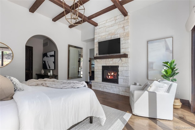 bedroom with a high ceiling, wood-type flooring, a fireplace, and beamed ceiling