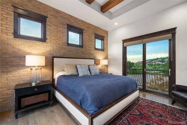 bedroom featuring access to outside, beam ceiling, hardwood / wood-style floors, and brick wall