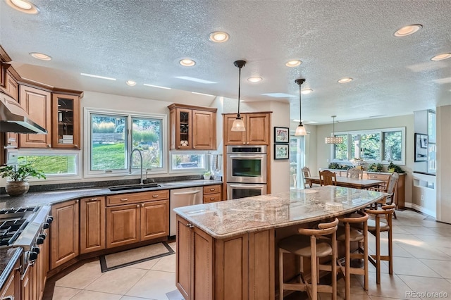 kitchen with a center island, stainless steel appliances, sink, hanging light fixtures, and a textured ceiling