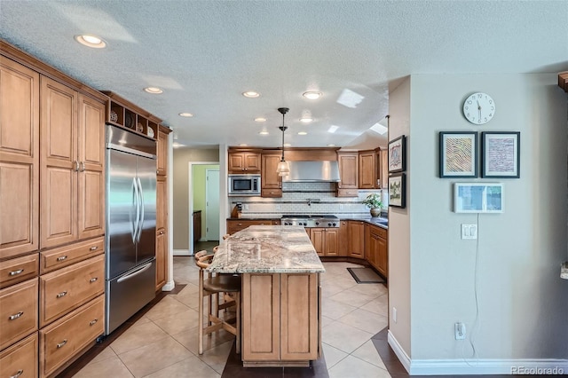 kitchen with a center island, a breakfast bar, tasteful backsplash, wall chimney range hood, and built in appliances