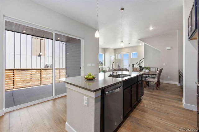 kitchen featuring stainless steel dishwasher, a sink, light wood-style flooring, baseboards, and an island with sink