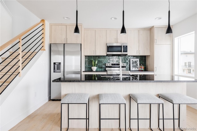 kitchen featuring a breakfast bar, hanging light fixtures, appliances with stainless steel finishes, an island with sink, and dark stone countertops