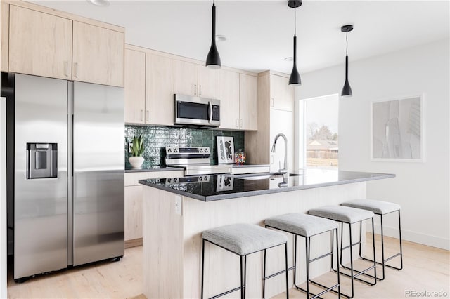 kitchen featuring light brown cabinets, a kitchen island with sink, a sink, hanging light fixtures, and appliances with stainless steel finishes