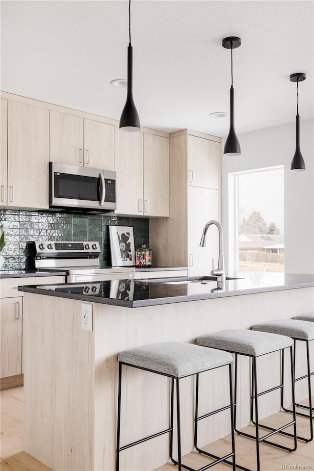 kitchen with stainless steel appliances, light brown cabinets, and pendant lighting