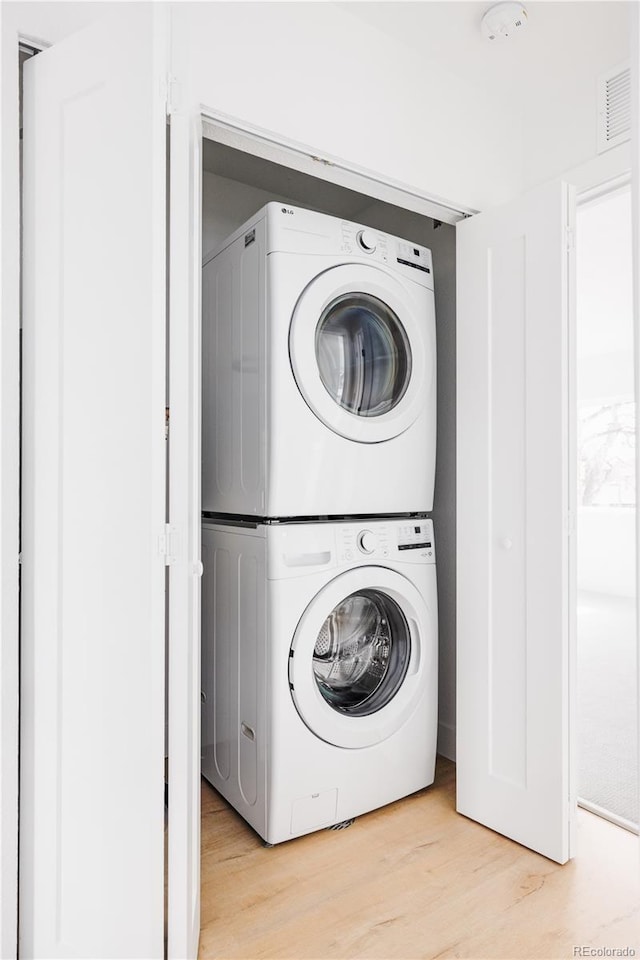 laundry room featuring laundry area, light wood-style flooring, visible vents, and stacked washer / drying machine