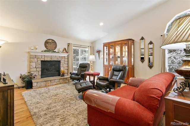 living room with a stone fireplace, light hardwood / wood-style floors, and vaulted ceiling