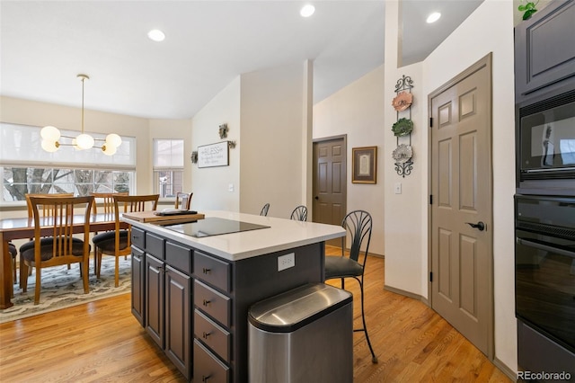 kitchen featuring a breakfast bar area, hanging light fixtures, a kitchen island, light hardwood / wood-style floors, and black appliances