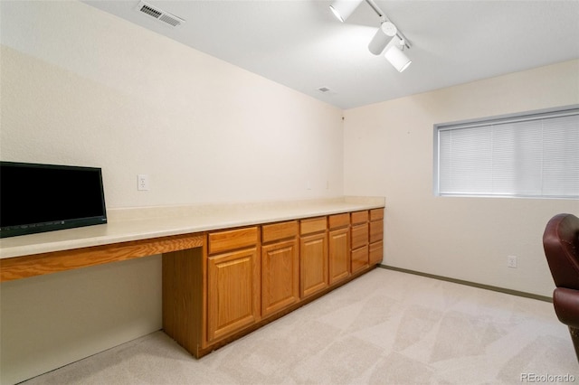 home office with built in desk, light colored carpet, and track lighting