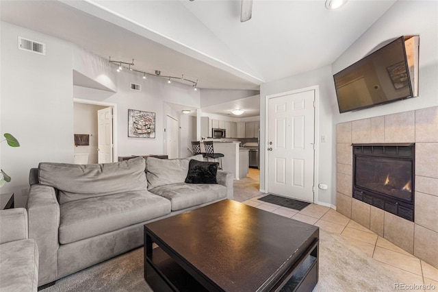 living room featuring a tiled fireplace, vaulted ceiling, rail lighting, and visible vents