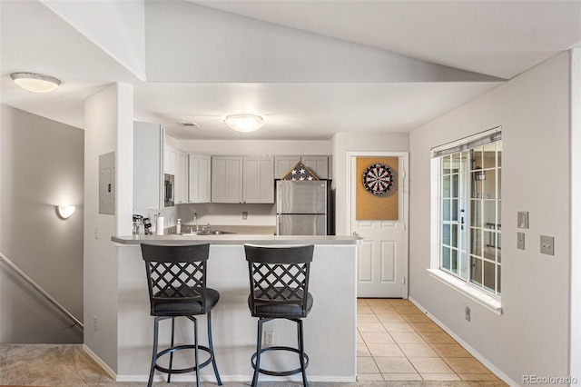 kitchen featuring light countertops, light tile patterned floors, a peninsula, a kitchen breakfast bar, and stainless steel appliances