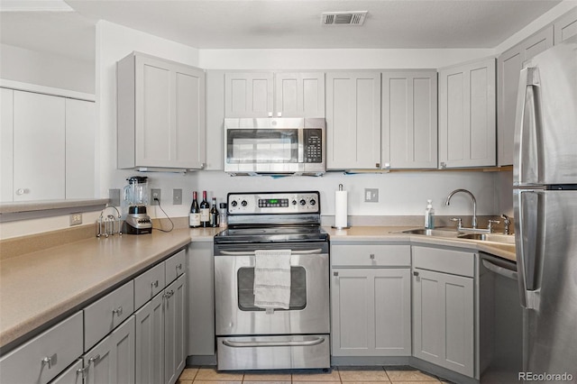 kitchen with visible vents, gray cabinetry, light countertops, stainless steel appliances, and a sink