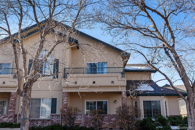 exterior space with a balcony, brick siding, and stucco siding