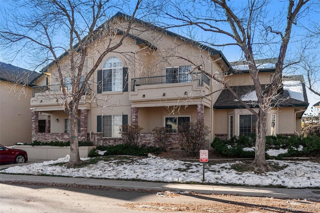 view of front of house featuring a balcony, brick siding, and stucco siding