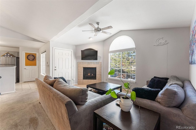 living area featuring vaulted ceiling, light colored carpet, a ceiling fan, and a tile fireplace