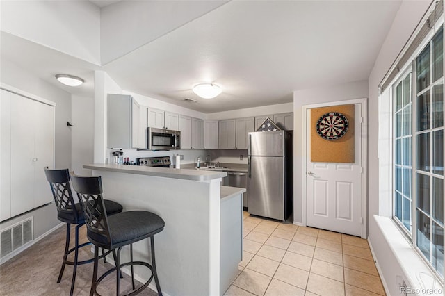 kitchen with appliances with stainless steel finishes, gray cabinets, a breakfast bar, light countertops, and a peninsula