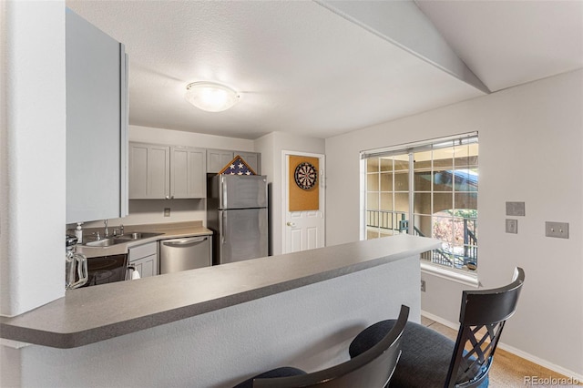 kitchen featuring stainless steel appliances, baseboards, a peninsula, a kitchen bar, and a sink