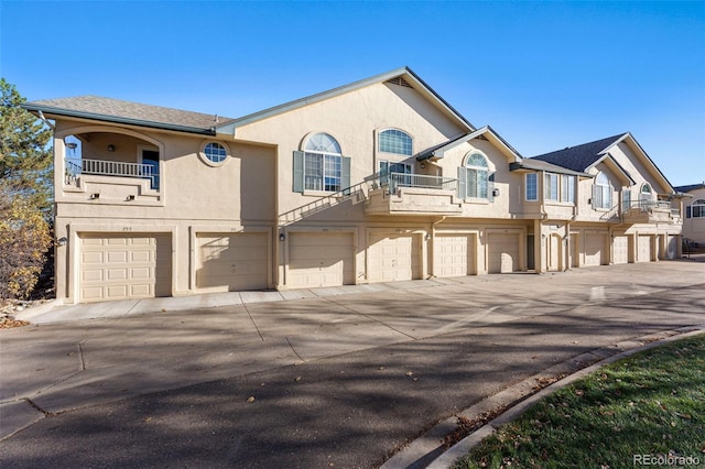 townhome / multi-family property featuring a balcony, an attached garage, stucco siding, and driveway