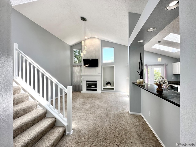 unfurnished living room with stairs, lofted ceiling with skylight, plenty of natural light, and carpet flooring